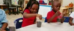 Kids sitting on a table in school playing with dirt in a cup.